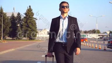 年轻的成功商人戴着太阳镜在日落时带着行李<strong>去机场</strong>候机楼。 一个英俊自信的男人